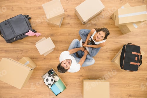 Preview: The happy couple sit near carton boxes and look to the camera. view from above