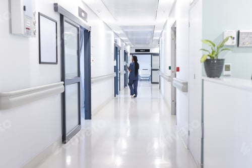 Preview: Back of african american female doctor with documents walking in hospital corridor