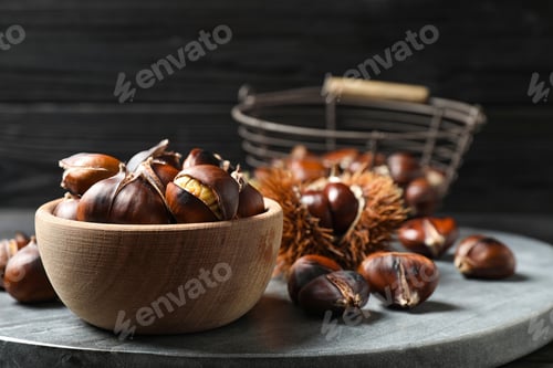 Preview: Delicious roasted edible chestnuts in wooden bowl on grey marble board, closeup