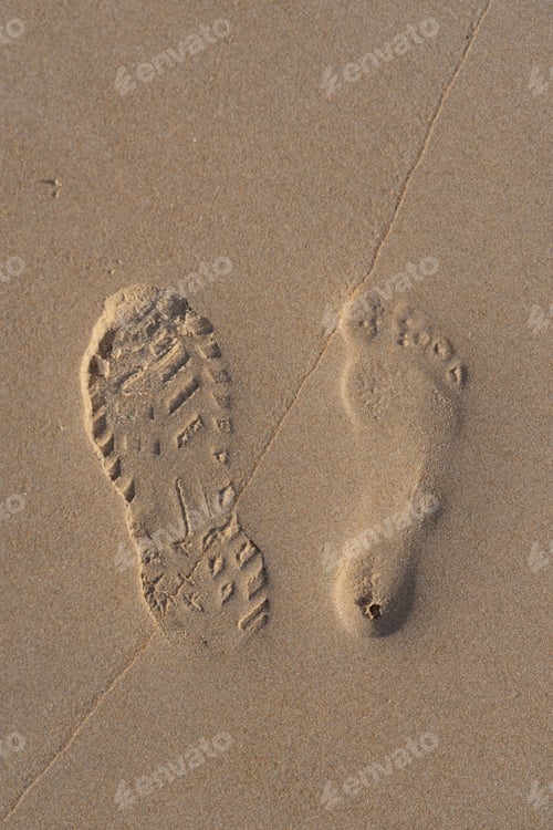 Preview: Footprint of a sneaker in the sand on the beach and another footprint of a bare foot next to it