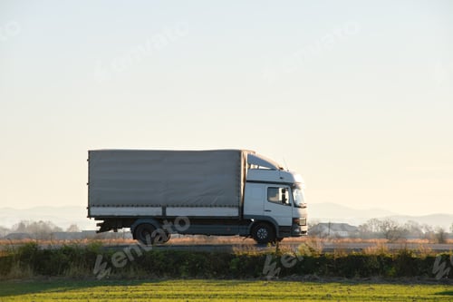 Preview: Cargo truck driving on highway hauling goods in evening.