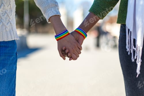 Preview: Interracial lesbian couple holding hands wearing rainbow bracelets, lgbtq plus love and equality