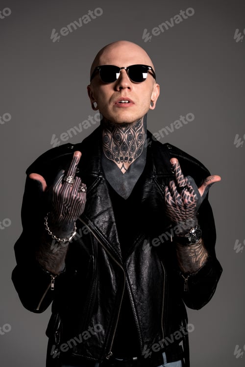 Preview: bald tattooed man in leather jacket and sunglasses showing middle fingers isolated on grey