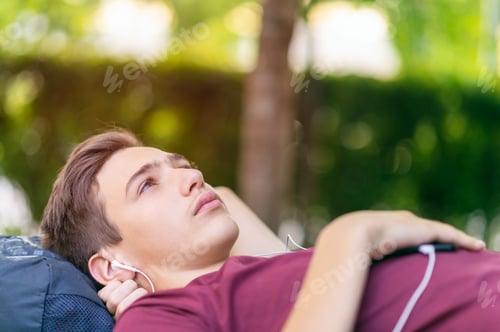 Preview: Close-up portrait of a sad young man lying on the bench in the park.