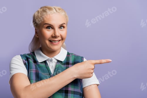 Preview: Cheerful student in vest and shirt pointing with finger isolated on purple