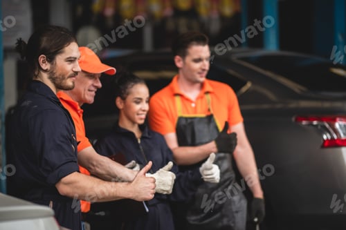 Preview: Group of young and senior car mechanics in garage wearing uniform enjoying and celebrating