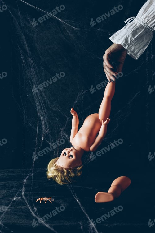 Preview: partial view of scary woman holding creepy doll in darkness with spider web