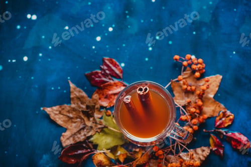 Preview: Tea cup with anise stars and cinnamon on a wet autumn background with fallen leaves and berries