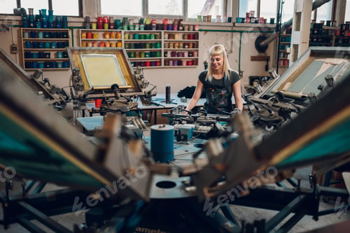 Preview: Graphic worker adjusting carousel screen printing machine at print shop