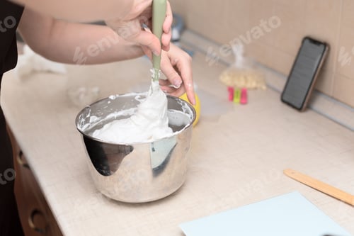 Preview: Woman whipping egg whites with manual whisk in bowl making meringue cake Pavlova