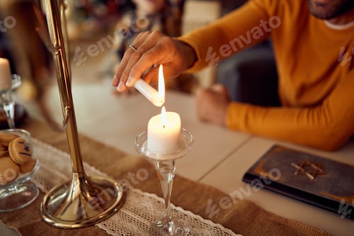 Preview: Close-up of man lightning up a candle while celebrating Hanukkah at home.