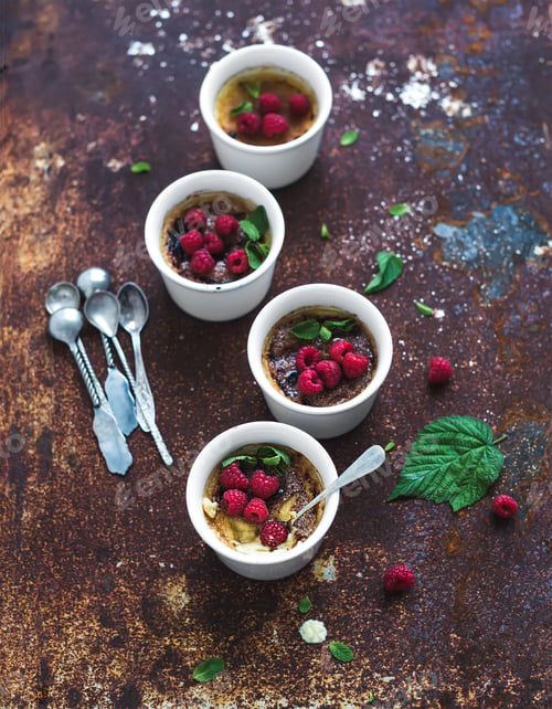 Preview: Creme brulees with raspberries and mint in white bowls over grunge metal backdrop. Top view