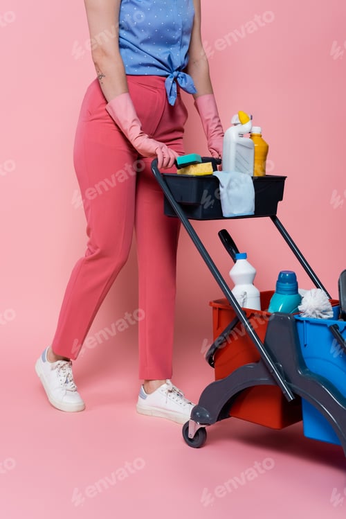Preview: cropped view of tattooed woman in rubber gloves standing near housekeeping cart with cleaning