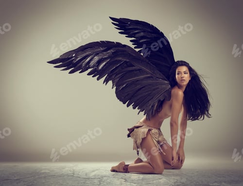 Preview: Dark angel of beauty. Shot of a woman with wings kneeling against gray background.