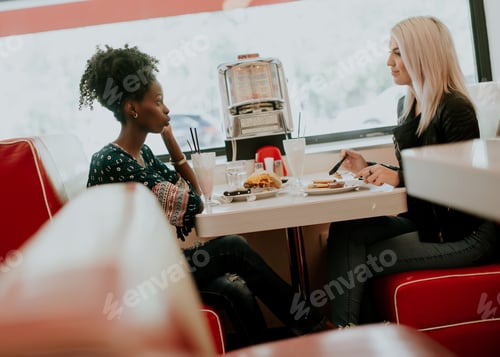 Preview: Multiracial female friends eating fast food at a table in the diner