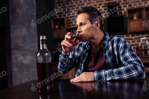 Preview: man with glass of alcohol sitting at table in kitchen at home