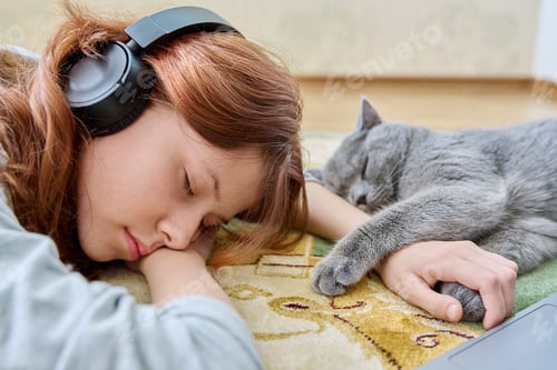 Preview: Preteen girl in headphones sleeping with cat on floor at home