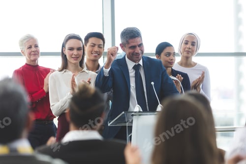 Preview: Businessman standing with diverse colleagues while speaking at business seminar in office building