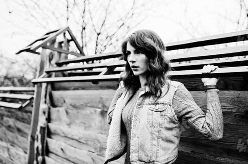 Preview: Portrait of brunette curly girl in jeans jacket against wooden wall.