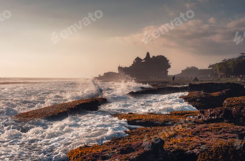 Preview: Pura Tanah Lot temple on clifftop and wave hitting on sunset beach in Bali