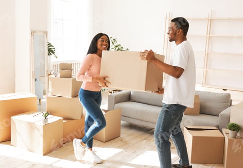 Preview: Full length of young black man with his girlfriend carrying cardboard box in their new home on
