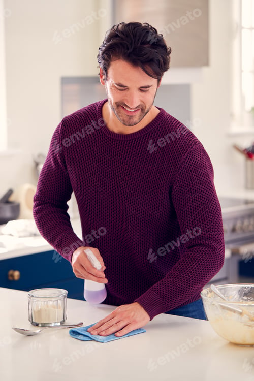 Preview: Man Cleaning Kitchen Counter With Spray And Cloth After Cake Baking