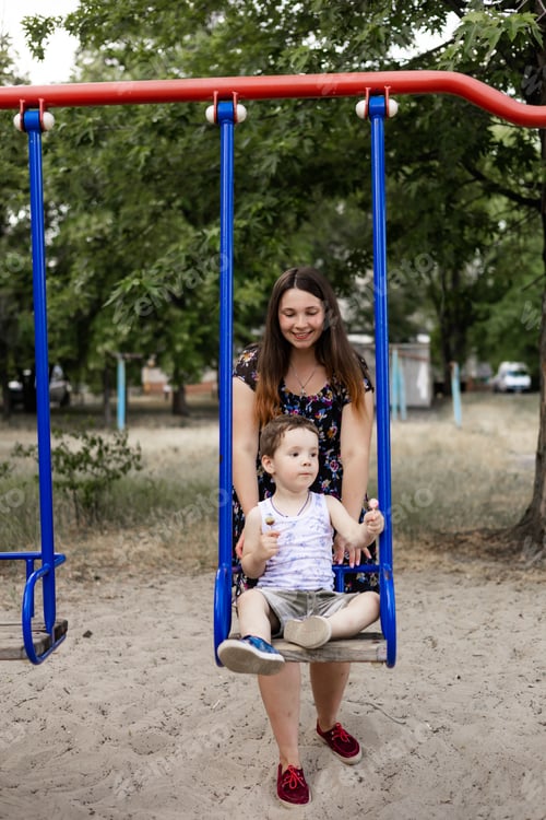 Preview: Mom swinging her baby boy in swing outdoor. Mother and her child having fun together outdoor. Happy