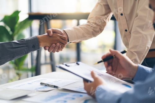 Preview: Entrepreneurs collaboration deal shaking hands in a modern office and financial paper graph on desk.