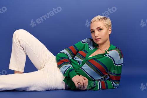 Preview: Young woman in stylish outfit poses against vibrant blue backdrop in creative studio setting