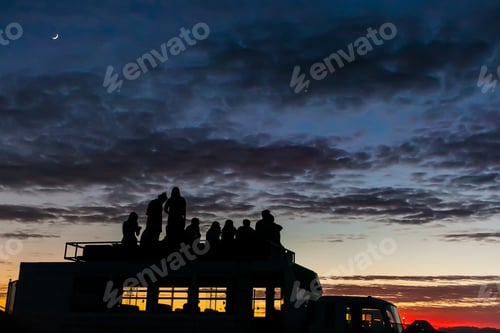 Preview: Beautiful shot of a silhouette of a group of friends watching the sunset on the car roof