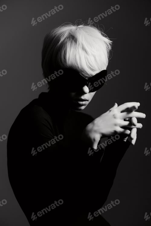 Preview: Mysterious woman with short blonde hair wearing oversized sunglasses, posed dramatically in black
