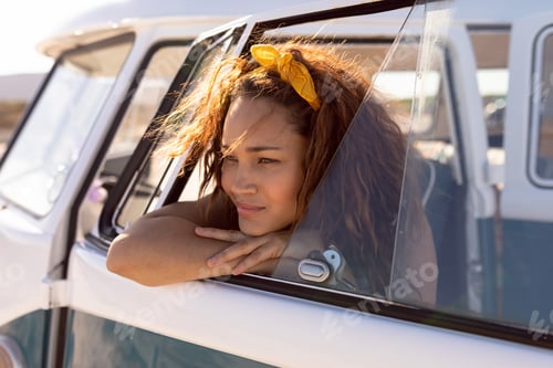 Preview: Side view of thoughtful young Mixed-race woman leaning on window of camper van at beach