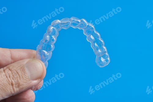 Preview: Clear Dental Aligner Held by a Hand Against a Bright Blue Background