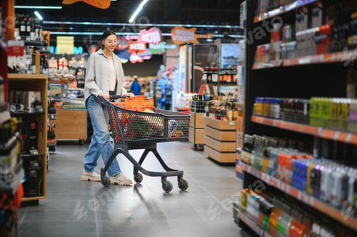 Preview: Pretty young woman in casual clothes chooses wine in the supermarket