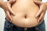 Vorschau: Übergewichtige asiatische Frau zeigt und drückt mit der Hand den fetten Bauch zusammen.