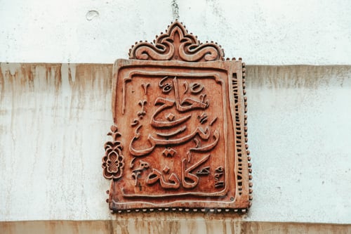 Preview: Metallic board with Arabic hieroglyphs on a textured wall with stains