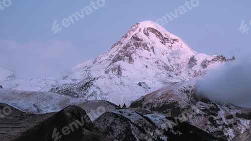 Preview: Stepantsminda, Gergeti, Georgia. Mount Kazbek Covered Snow In Winter Sunrise. Morning Dawn Colored