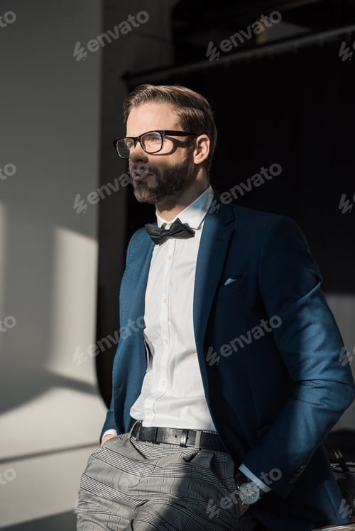 Preview: handsome stylish young businessman in eyeglasses and bow tie looking away