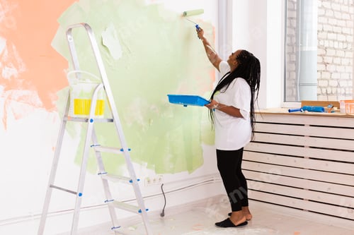 Preview: Beautiful african american girl painting the wall with paint roller. Portrait of a young beautiful