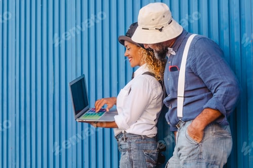 Preview: Portrait smiling handsome adult couple leaning outdoor against blue metal panel using laptop