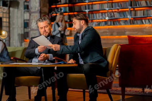 Preview: in the office the director sits with a business partner discussing a deal and reading documents
