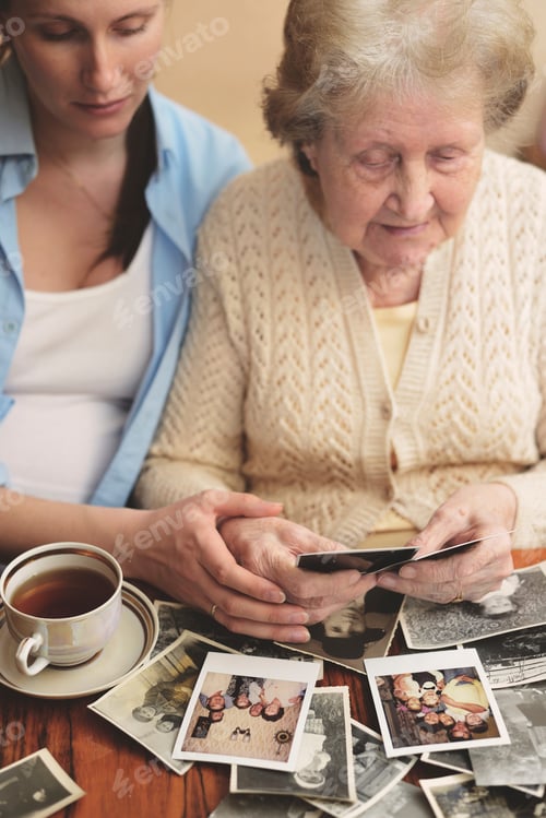 Preview: Senior woman and granddaughter sitting at table, looking through old photographs
