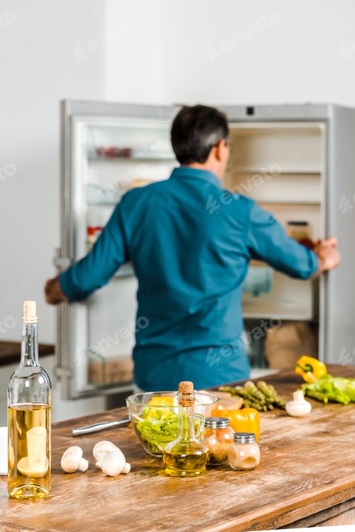 Preview: back view of mature man looking into fridge in kitchen