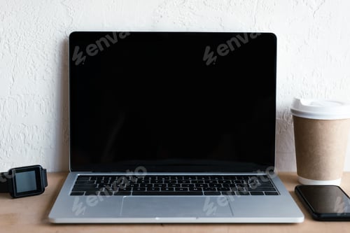 Preview: laptop with blank screen, smartwatch, smartphone and coffee to go on table