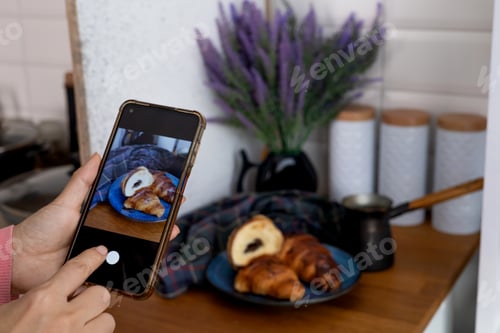 Preview: Woman taking picture of breakfast in cafe. Croissant, coffee with cream and jam on wooden table. Ton