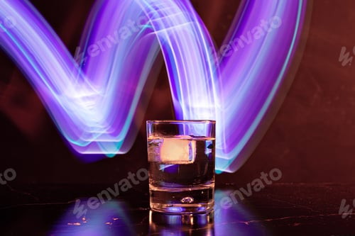 Preview: whiskey glass with ice on black backgound with neon light painings behind