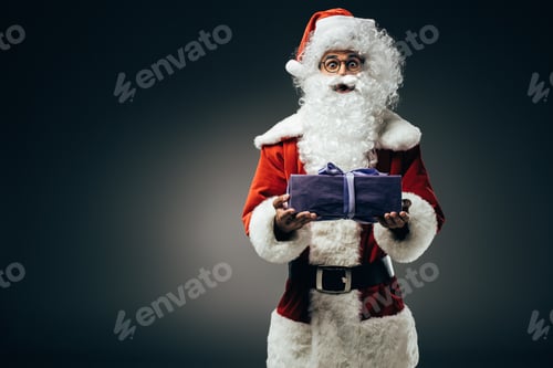 Preview: surprised santa claus in costume holding gift box isolated on grey background