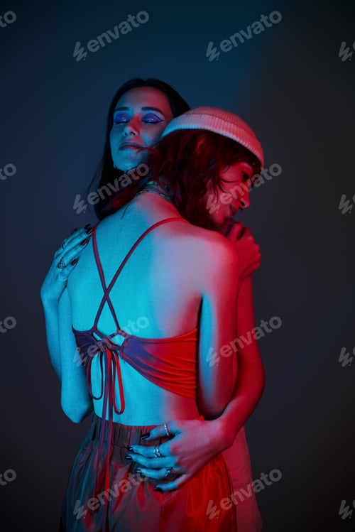 Preview: young lgbt couple with bold makeup and stylish attire hugging under purple lights in studio