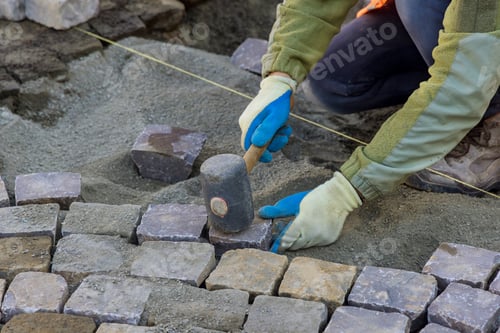Preview: Worker using rubber hammer to laying pavement stones on sidewalk near road in city