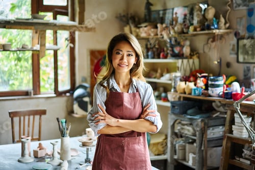 Preview: Pretty female artist smiling and posing at creative workshop with her artwork in the background.